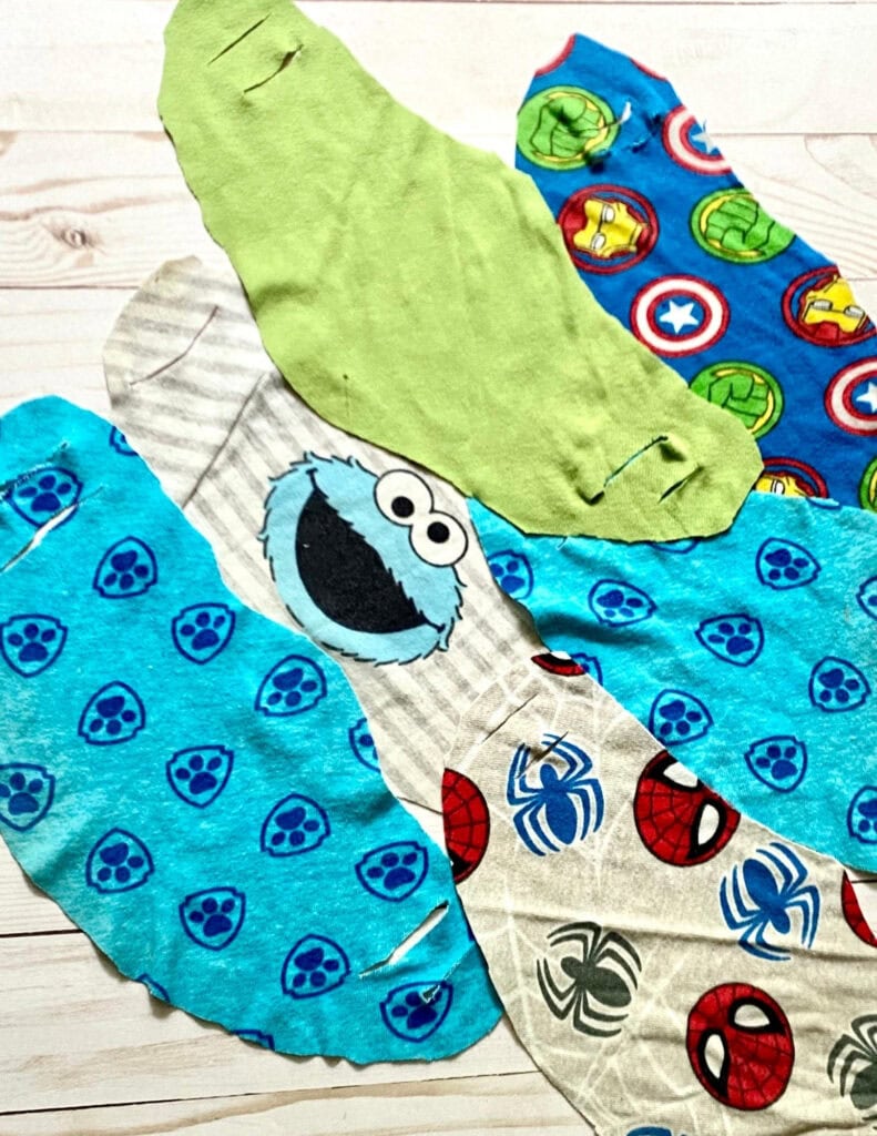Colorful superhero-themed fabric gift wraps featuring Marvel characters like Spider-Man, Captain America, Iron Man, Hulk, and others arranged on a light wood background for eco-friendly gift wrapping.