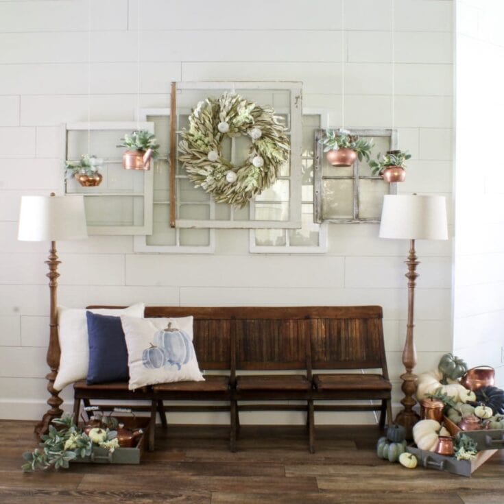 Rustic fall decor with pumpkins, greenery, and accent pillows on a wooden bench, perfect for cozy autumn welcomes.