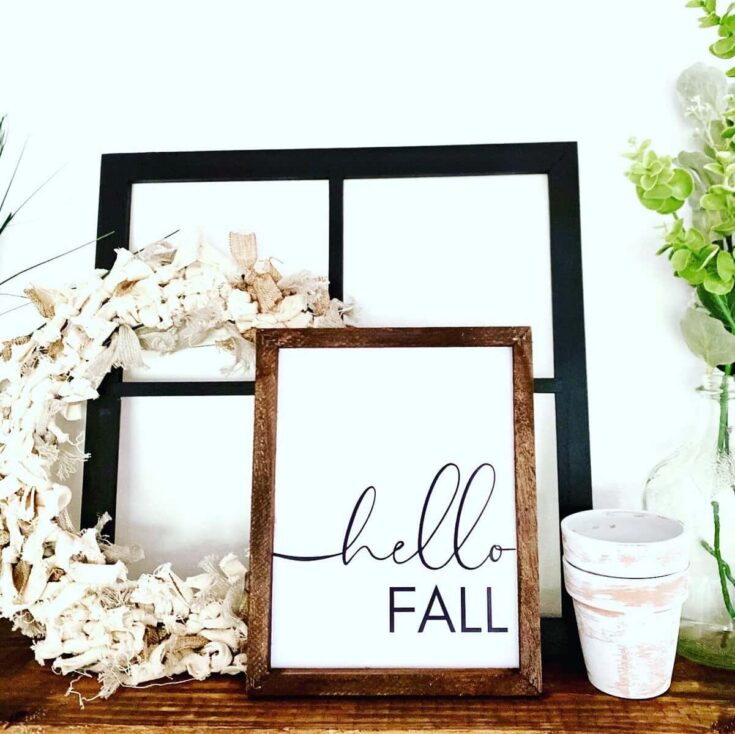 Cozy fall decor with a rustic "hello fall" sign, dried white flowers, green plants, and white flower pots, creating a warm seasonal home ambiance.