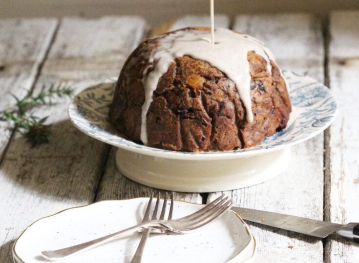 Moist fruitcake with white icing drizzle served on a decorative plate, rustic background, cozy holiday or special occasion dessert.