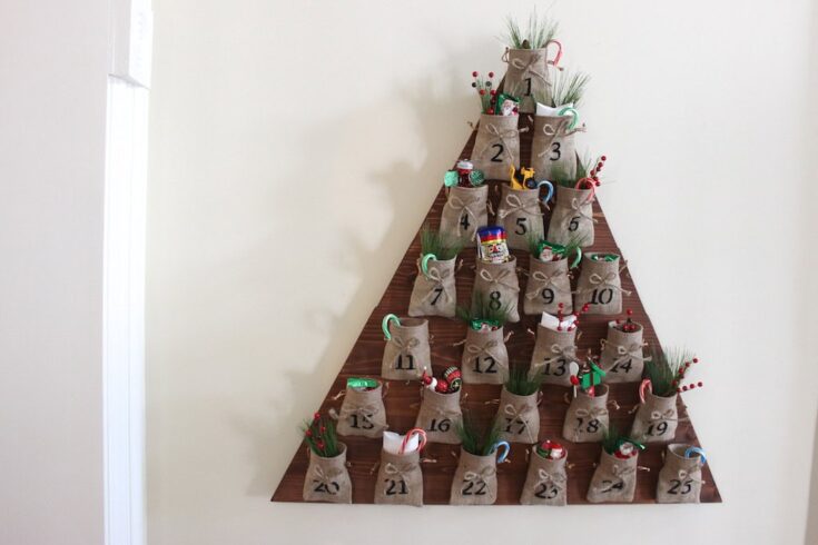 Stacked burlap pouch Christmas advent calendar with small gifts and greenery, arranged in a festive triangle for holiday countdown and decoration.