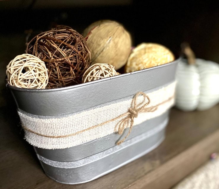 Rustic decorative metal container filled with natural wicker balls, adorned with a burlap ribbon, perfect for home decor and creating cozy, farmhouse-inspired interior design.