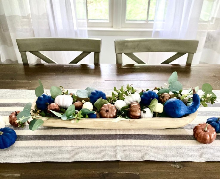 Vibrant fall decorative pumpkins and eucalyptus arranged on a wooden tray on a dining table with striped table runner, perfect for autumn decor.