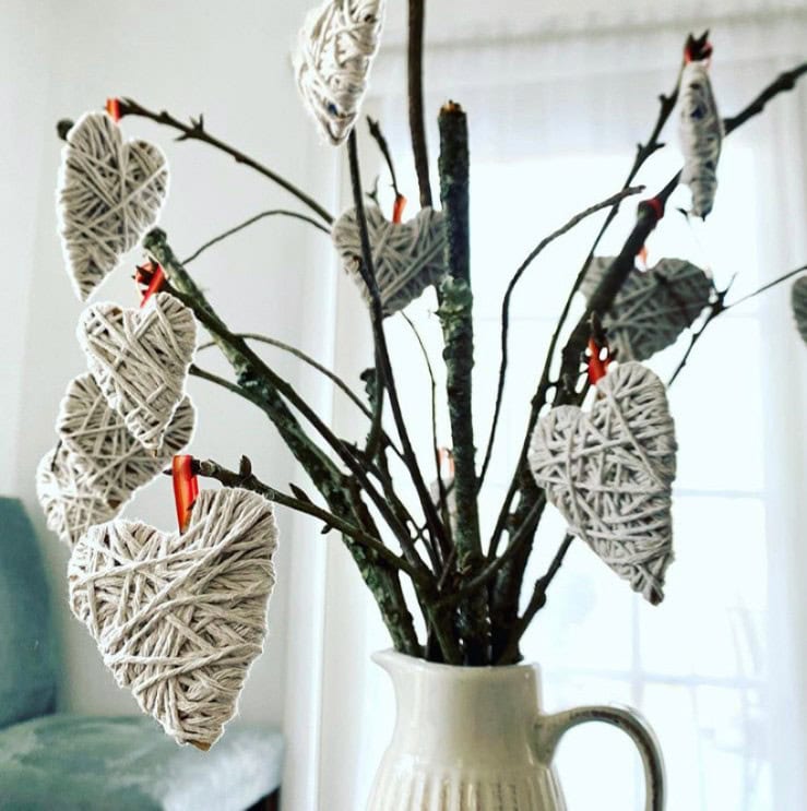 Heart-shaped wicker ornaments handmade with string, displayed on tree branches in a white vase.