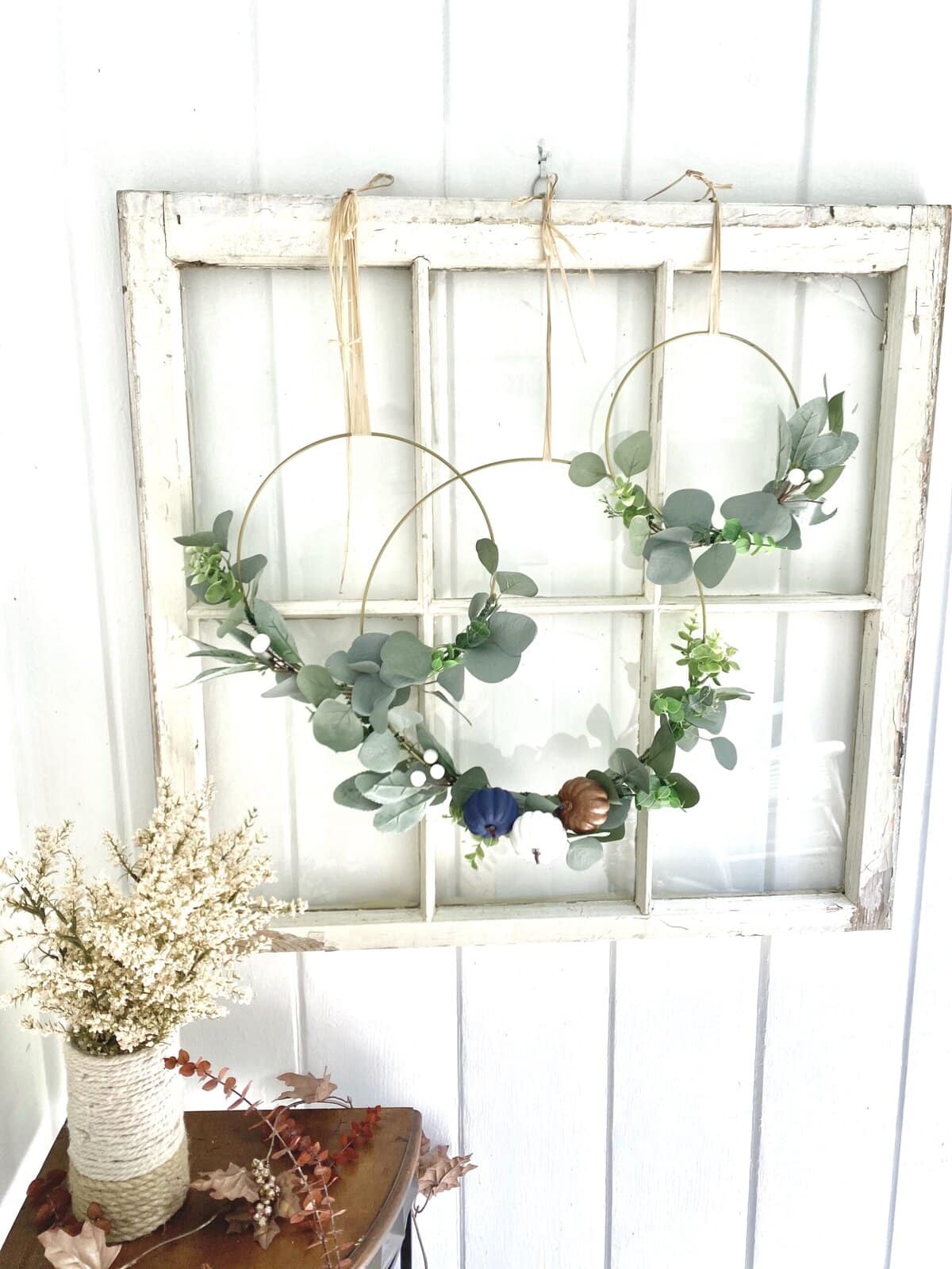 Delicate eucalyptus wreath wall decor with faux flowers, perfect for rustic or modern home accents. Handcrafted plant arrangement on distressed wooden backdrop.