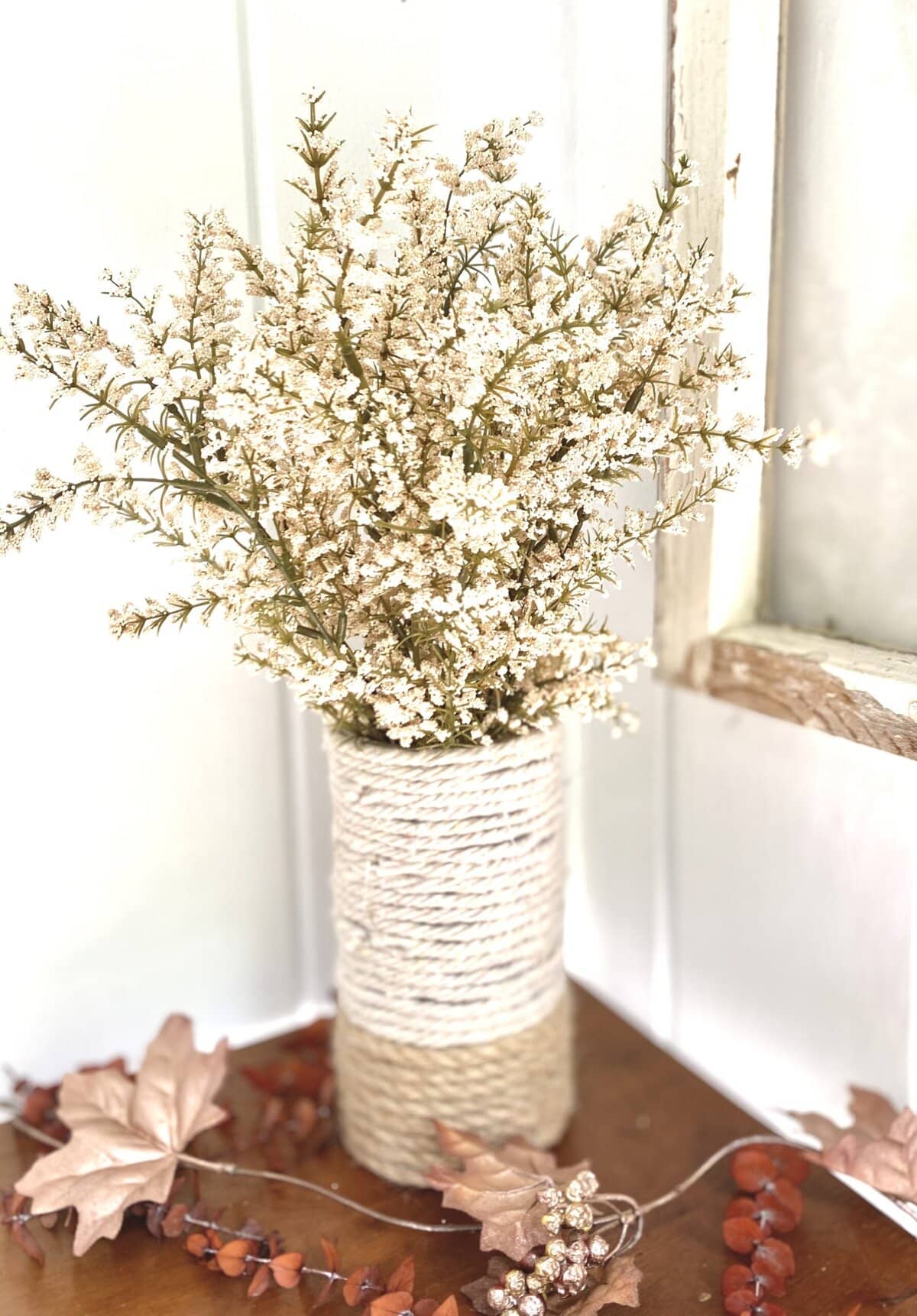 Rustic white vase with dried floral arrangement, neutral tones, decorative fall-inspired leaves and berries, elegant home decor, styled for cozy seasonal ambiance.