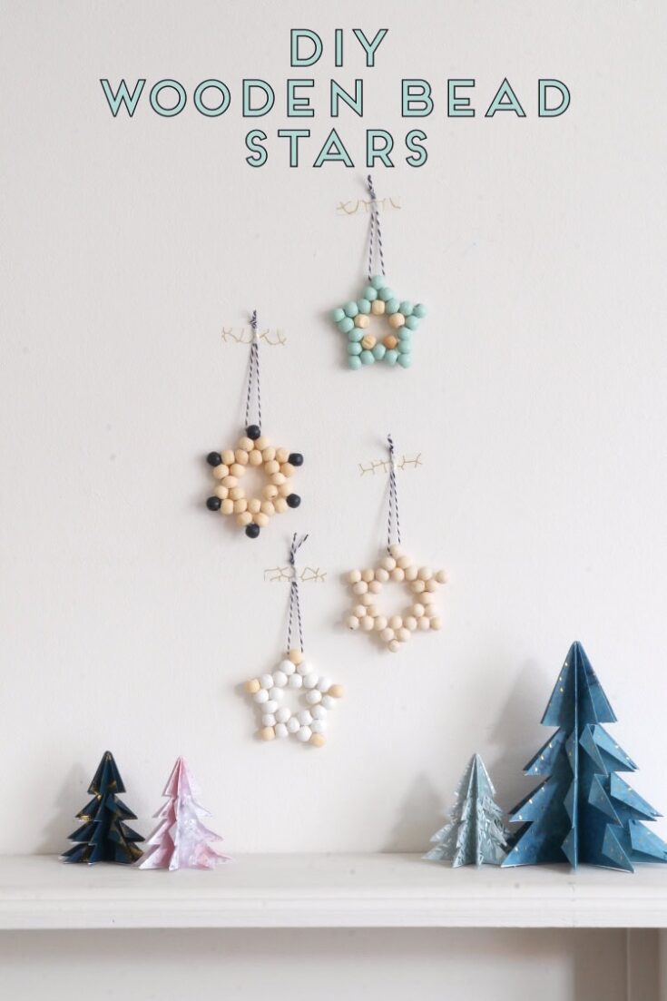 Colorful DIY wooden star bead ornaments hanging on a white wall, with paper Christmas trees below, perfect for holiday decorations and craft projects.