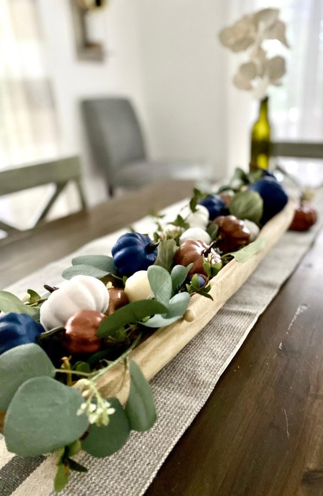 Colorful pumpkin fall decor on a wooden table with eucalyptus leaves for Thanksgiving or autumn celebration.