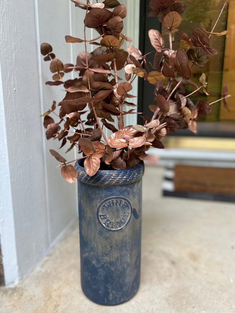 Silk bronze eucalyptus plant in a rustic blue vintage milk can vase, perfect for elegant home decor and adding a natural touch to living spaces.