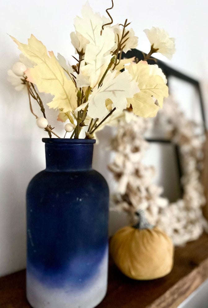 Blue and white ceramic vase with white faux autumn leaves and berries, fall decor centerpiece.