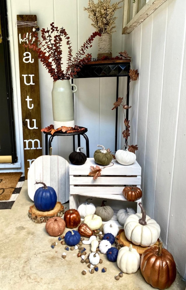 Pumpkin fall decor with painted and natural pumpkins in various colors and textures displayed in cozy autumn outdoor setting with decorative leaves and seasonal accents.