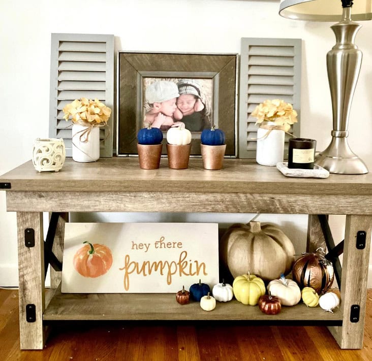 Small rustic wooden console table decorated with pumpkins, gourds, candles, and floral arrangements, creating a cozy fall decor display for home or seasonal occasions.