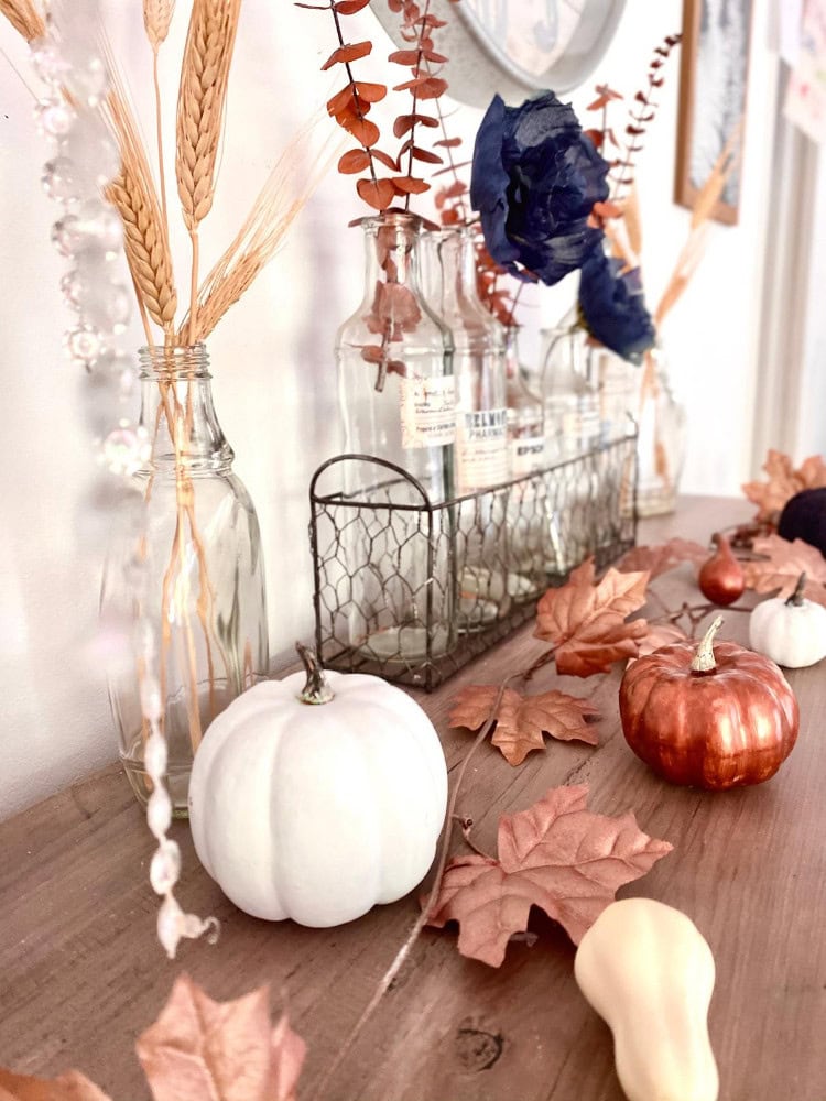 Pumpkin fall decor with dried leaves and elegant glass bottles, creating a cozy autumn atmosphere for home styling and seasonal celebrations.