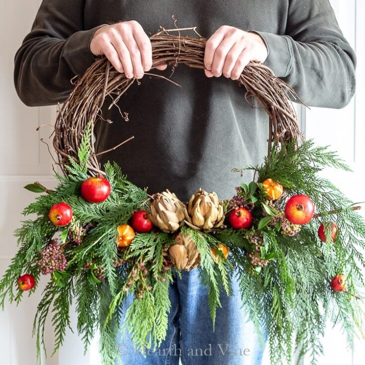 Red apple and artichoke Christmas wreath with fresh greenery and berries, autumn-inspired holiday decor, natural festive wreath for winter celebrations.