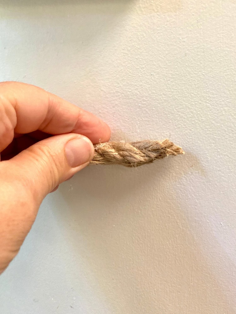 Twine being pulled on a beige wall, symbolizing rustic decor, home accents, or creative DIY projects with natural materials.
