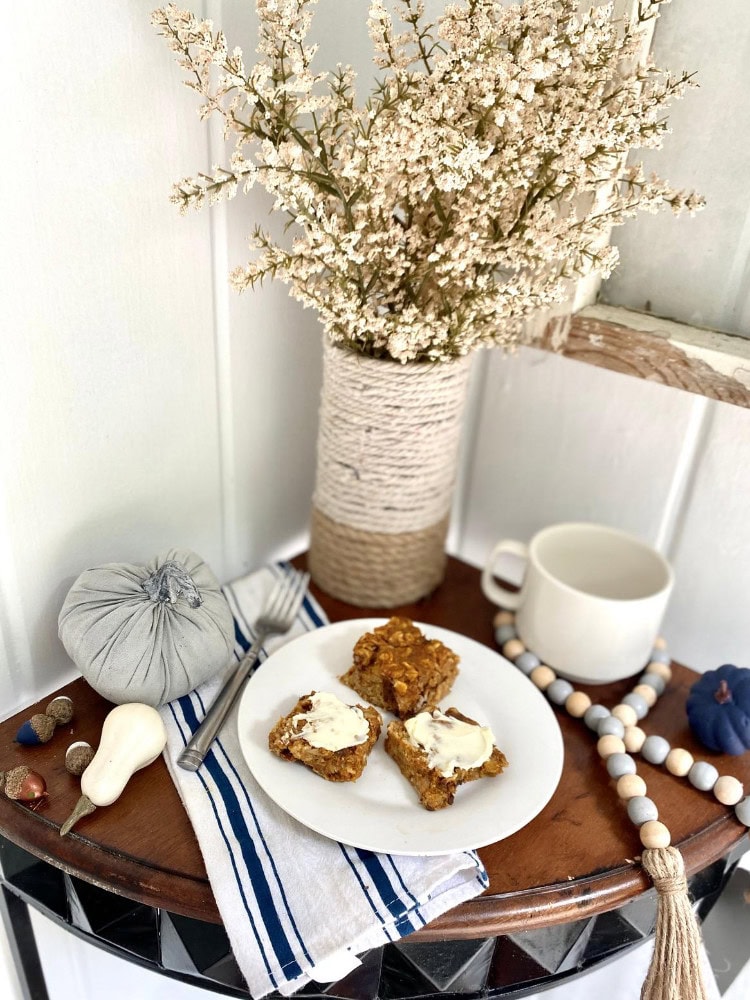 Sweet breakfast scene with homemade oatmeal cookie bars, a white mug, decorative pumpkins, and a vase of white flowers on a rustic wooden table, perfect for cozy mornings and farmhouse decor.