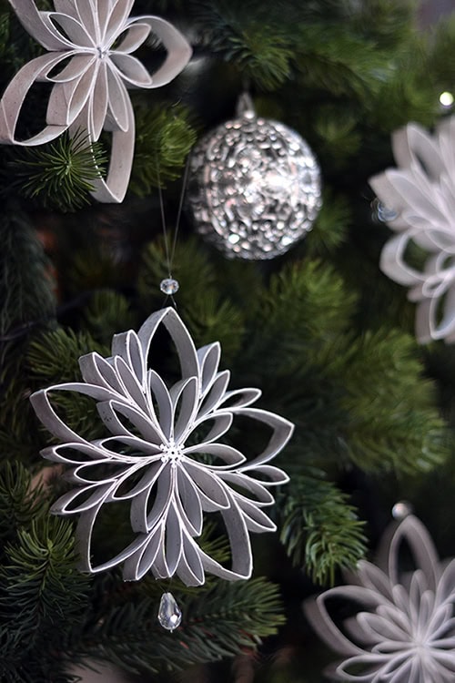 Silver snowflake Christmas ornament hanging on a decorated Christmas tree, with a shiny silver ball ornament in the background. Perfect holiday decor for a festive and elegant home.