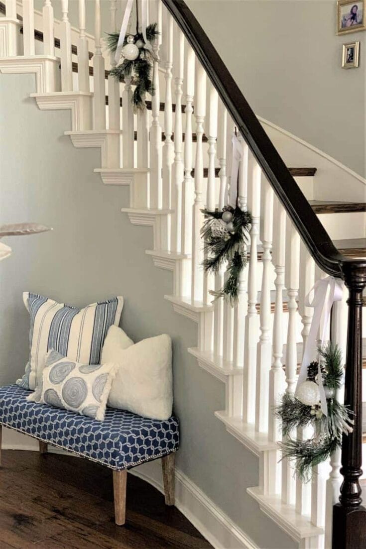 Decorated staircase with holiday garlands and ornaments, cozy bench with pillows under bright lighting, perfect for festive seasonal home decor.