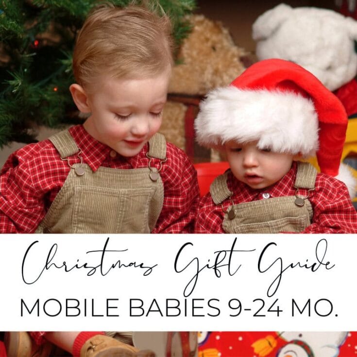 Cute toddlers in festive Christmas outfits, one wearing a Santa hat, sitting by a decorated tree, perfect for holiday gift guide for mobile babies 9-24 months.