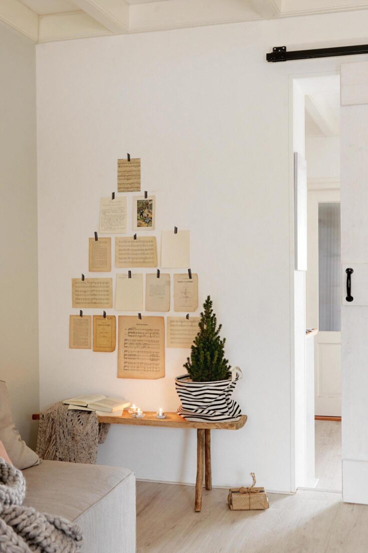 Vintage sheet music and nostalgic photos displayed on a white wall in a cozy, minimalist living space. Natural wood accents, candles, and a small potted Christmas tree add warmth and charm.