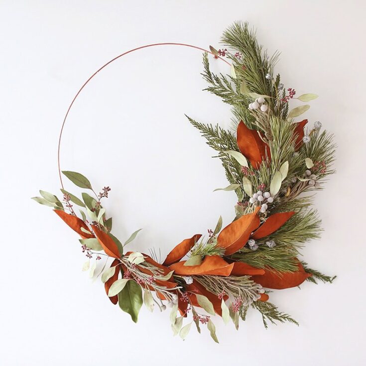 A festive holiday wreath featuring evergreen branches, eucalyptus leaves, and rust-colored decorative elements, perfect for Christmas or winter decor.