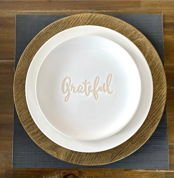 Grateful written on white ceramic plate with wooden charger, celebrating gratitude, mindfulness, and positive mindset for home decor or tabletop inspiration.