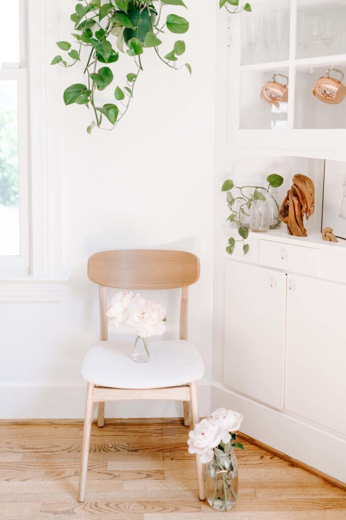 Delicate peonies in glass vases on a cozy chair with a minimalistic white interior, showcasing elegant home decor, floral accents, and natural wood elements for a serene, stylish space.