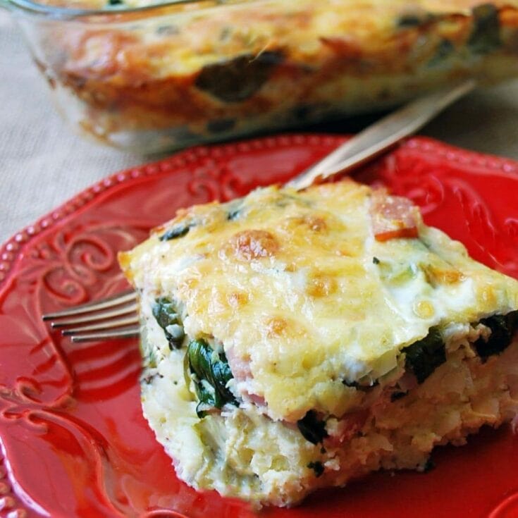 Baked spinach and cheese casserole slice served on a red decorative plate, with a whole casserole dish in the background, emphasizing homemade comfort food and healthy ingredients.