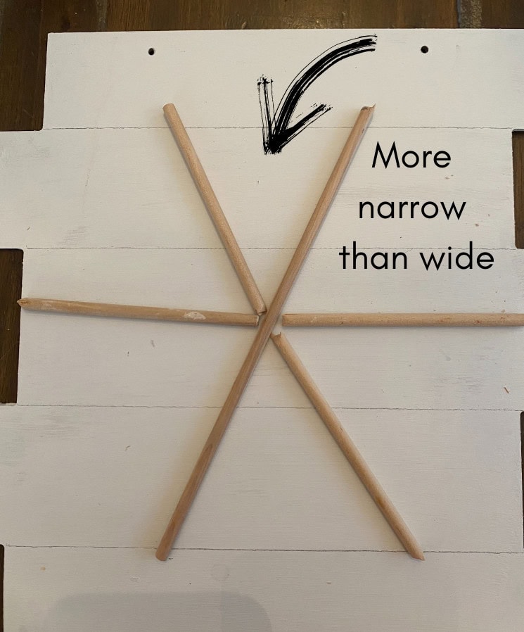 More narrow than wide wooden skewers arranged in a star pattern on white wooden background.