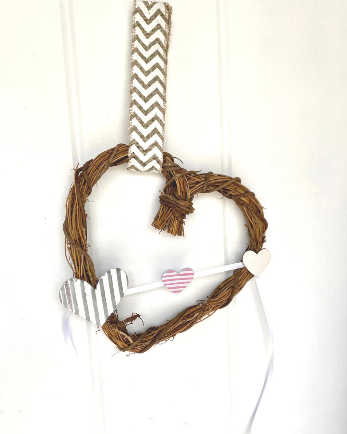 Heart-shaped wreath made of twisted twigs with decorative paper hearts and striped ribbon, ideal for romantic or rustic home decor, Valentine's Day, or craft projects.