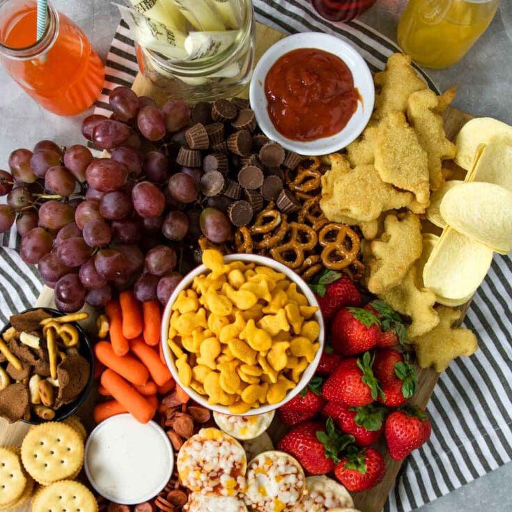 Fresh fruit and snack platter with strawberries, grapes, assorted candies, pretzels, chicken tenders, and dipping sauces for a family-friendly celebration. Perfect for gatherings and parties.