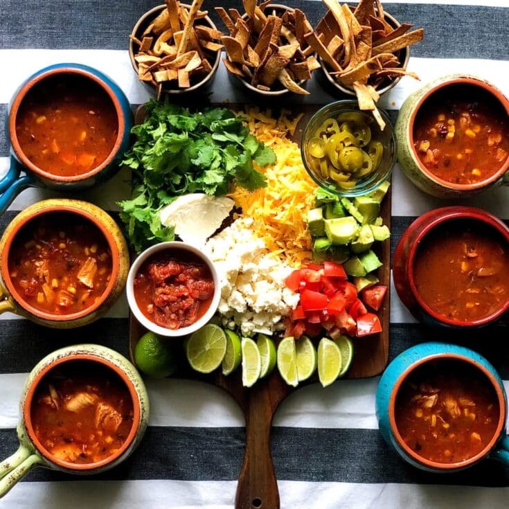 Fresh homemade Mexican tortilla soup with colorful vegetables, cilantro, cheese, lime, and crispy tortilla strips, served in vibrant bowls for a delicious, hearty meal.