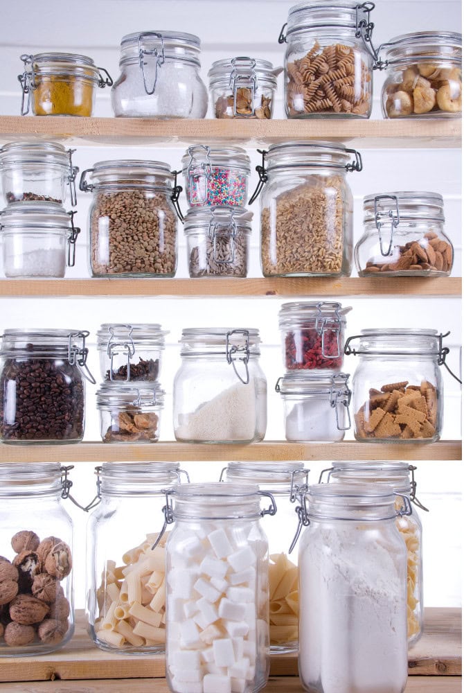 Colorful glass jars filled with baking ingredients organized on wooden shelves, showcasing a variety of sugars, flour, sprinkles, and candies for baking at A Hundred Affections.
