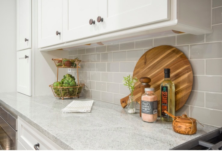 Fresh kitchen countertop with cutting board, salt, olive oil, greenery, and decorative elements in a clean, modern kitchen setting.