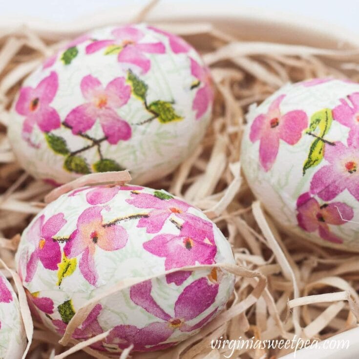 Pink floral patterned chocolate eggs nestled in straw for Easter decor or gifts.