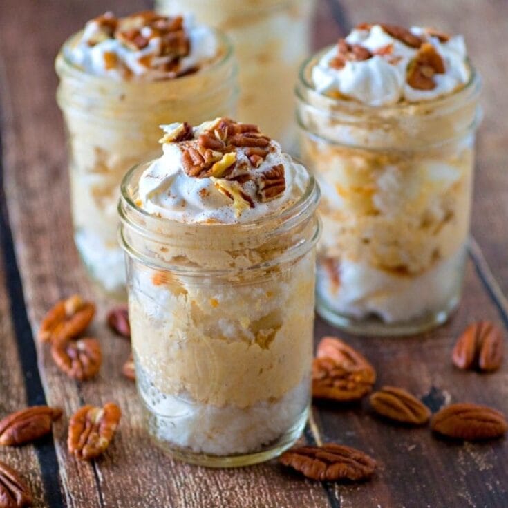Rich and creamy caramel pecan pudding in mason jars topped with whipped cream and chopped pecans, perfect for a comforting dessert or festive treat.
