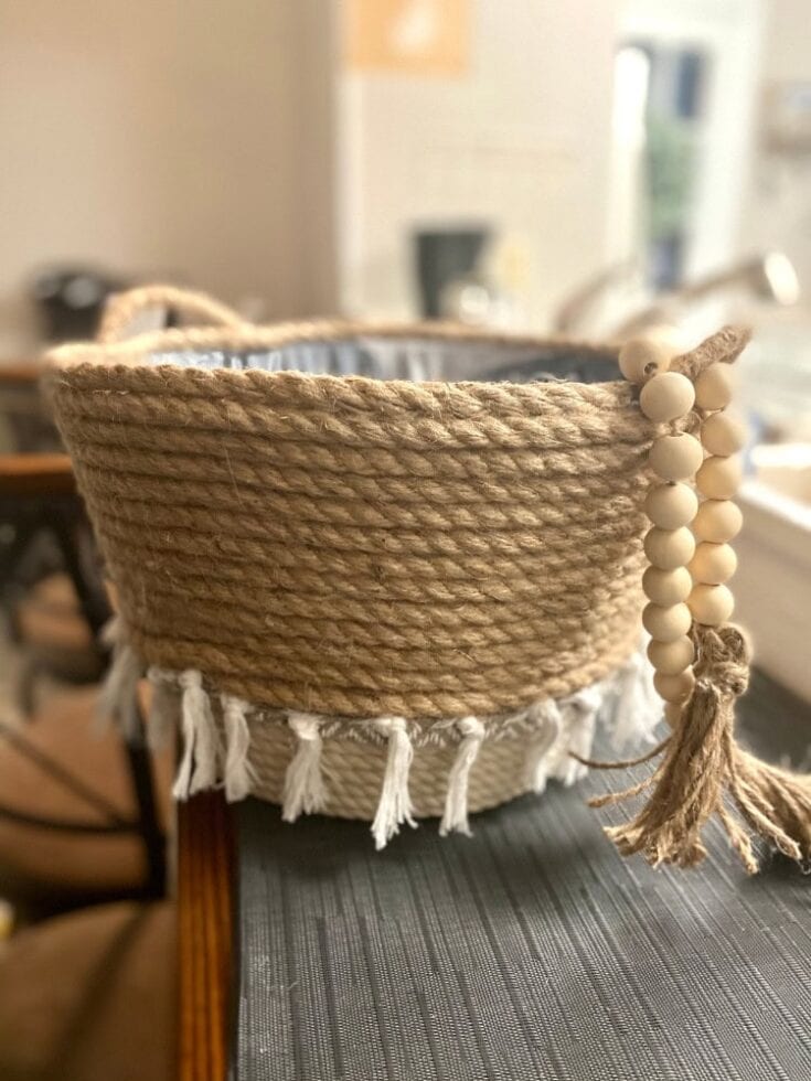 Natural jute rope basket with decorative white tassels and wooden bead accents, perfect for rustic and boho home decor.