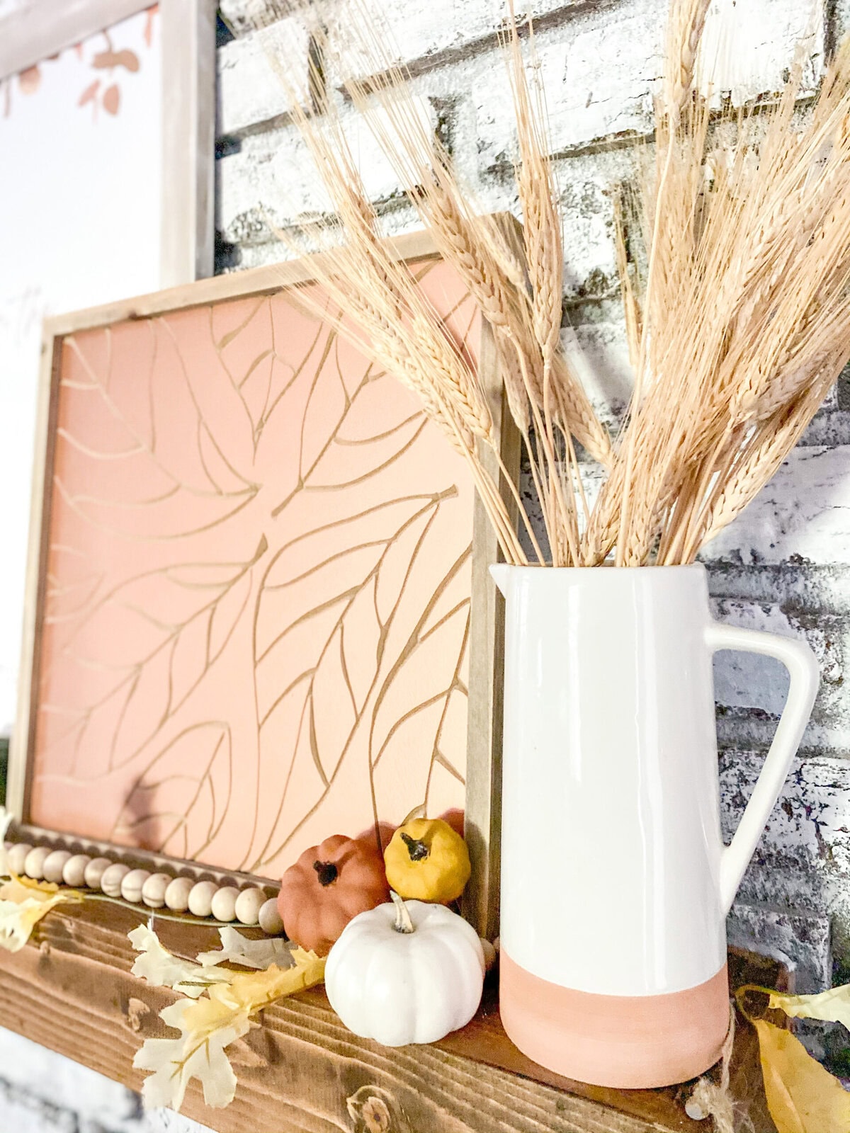 Soft pink and white autumn-inspired decor with wheat stalks, pumpkins, and natural elements in a cozy, rustic setting.