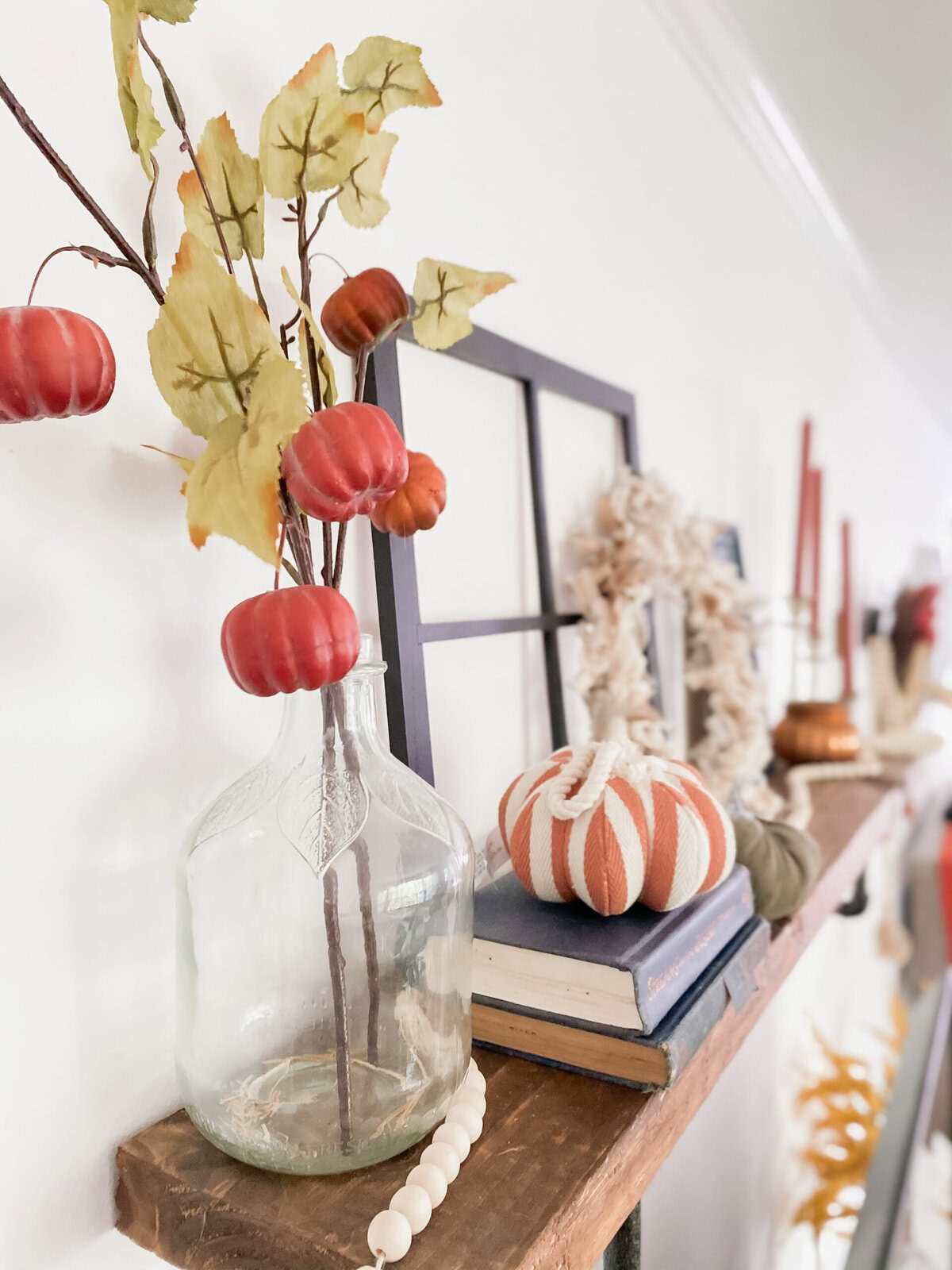 Vase with autumnal faux pumpkin and leaf arrangement for seasonal fall home decor, styled on a rustic wooden shelf with pumpkins and decorative accents.