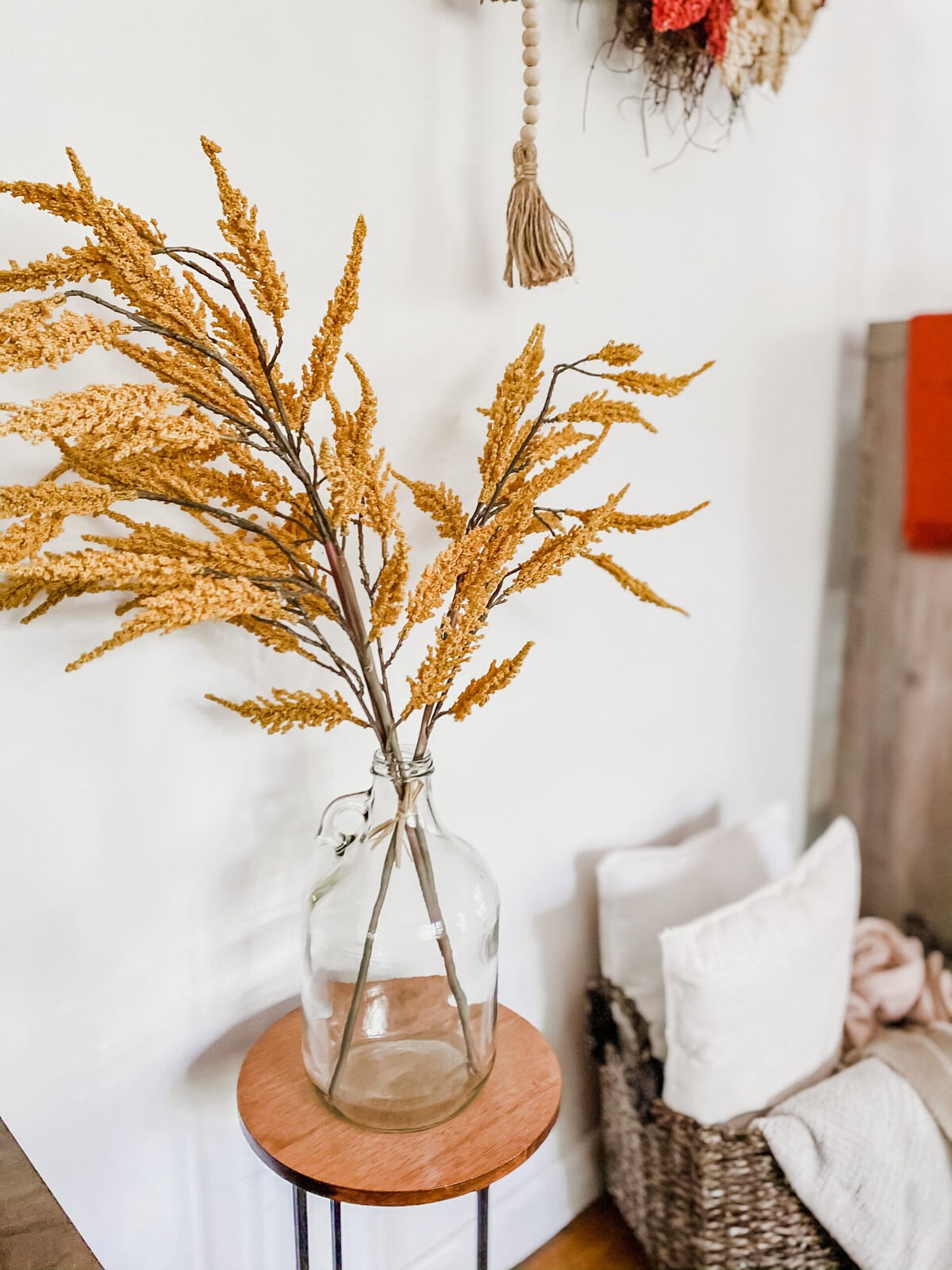 Dried golden wheat stems in a clear glass vase on a small wooden table, showcasing rustic home decor with natural accents.