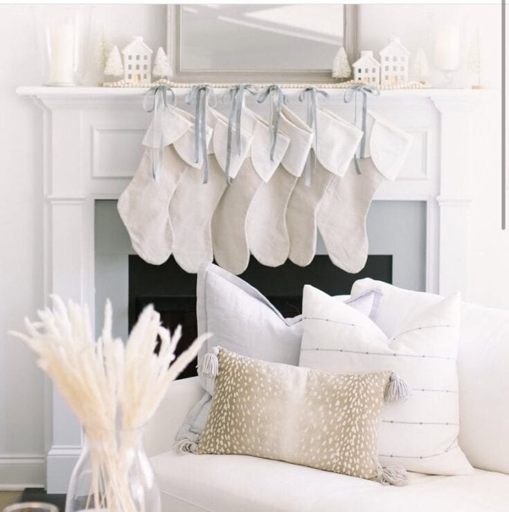 Plain white Christmas stockings hanging on a fireplace mantel, decorated with blue ribbons, in a cozy holiday home setting.