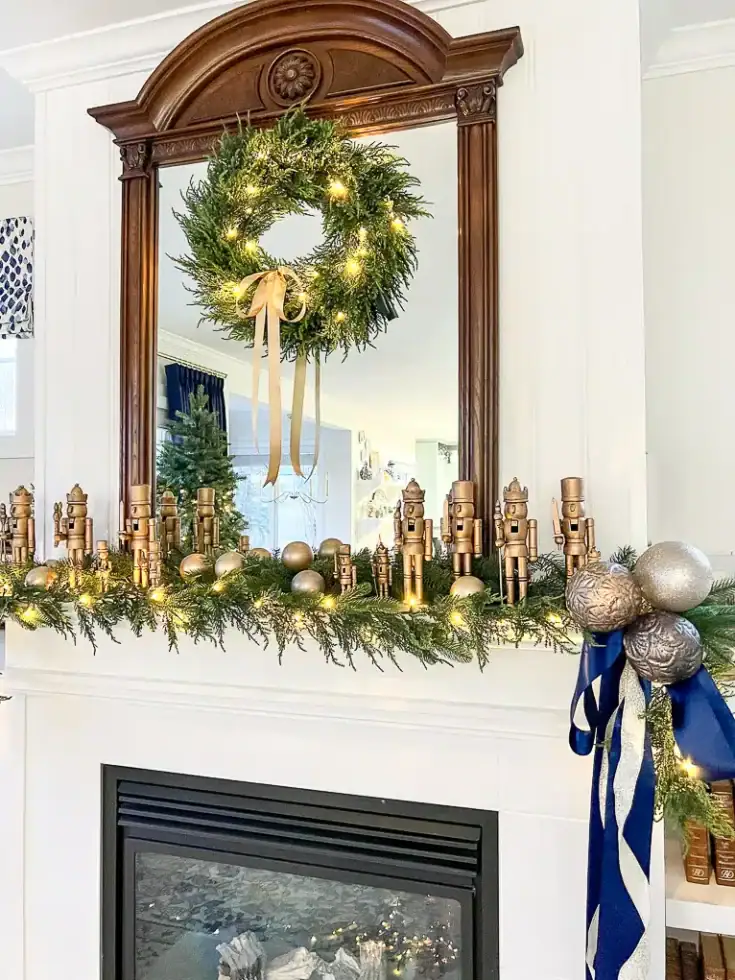 Festive Christmas fireplace mantel decorated with a lush green garland, gold ornaments, and a wooden nutcracker garland, topped with a wreath and warm lighting creating cozy holiday ambiance.