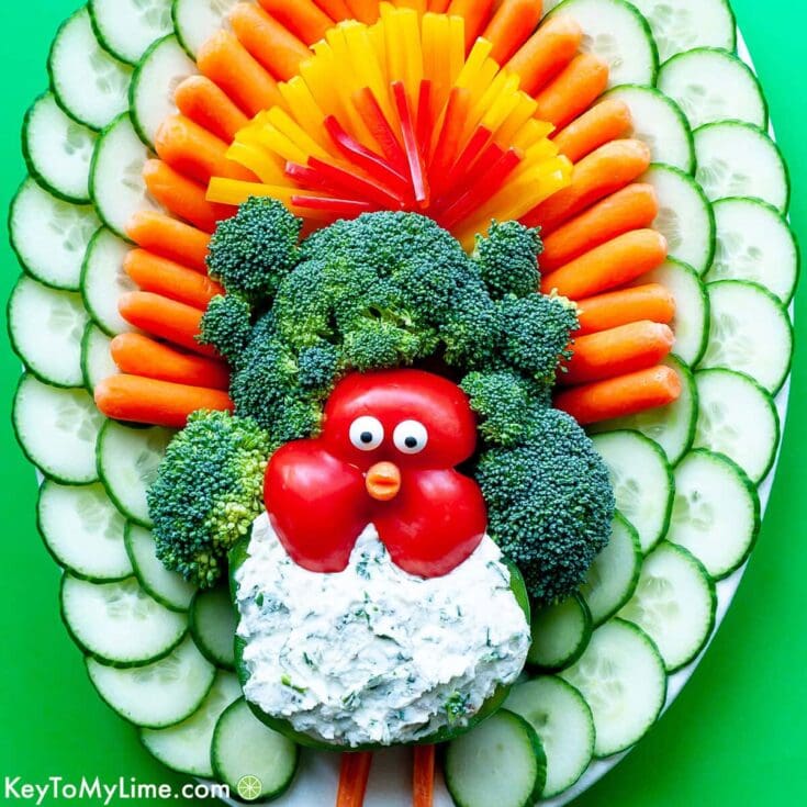 Broccoli and veggie platter with a playful turkey made from cherry tomatoes and a creamy dip, perfect for Thanksgiving or holiday parties. Featuring fresh cucumber, carrots, red and yellow bell peppers for colorful presentation.