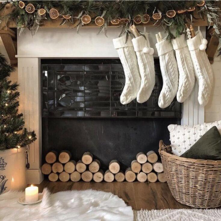 Fireplace with stockings and cozy Christmas decor, log storage, and festive greenery, creating a warm holiday living room scene.