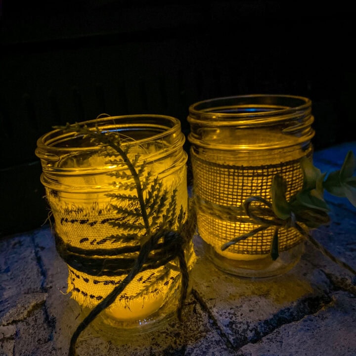 Soft glowing candles in mason jars wrapped with lace and twine, creating a cozy and romantic ambiance for home decor or outdoor events.