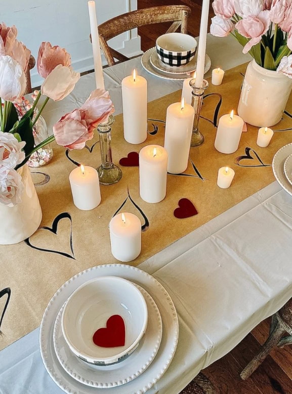 A romantic dinner table setup with lit candles, flowers, and heart motifs, perfect for intimate gatherings and special occasions by A Hundred Affections.