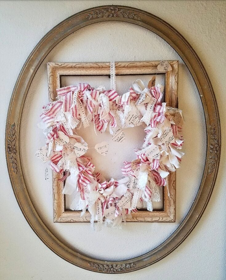 Vintage shabby chic fabric and paper heart wreath with lace and ribbon accents, displayed inside a rustic wooden frame and an ornate oval mirror, perfect for romantic home decor and handcrafted wall art.