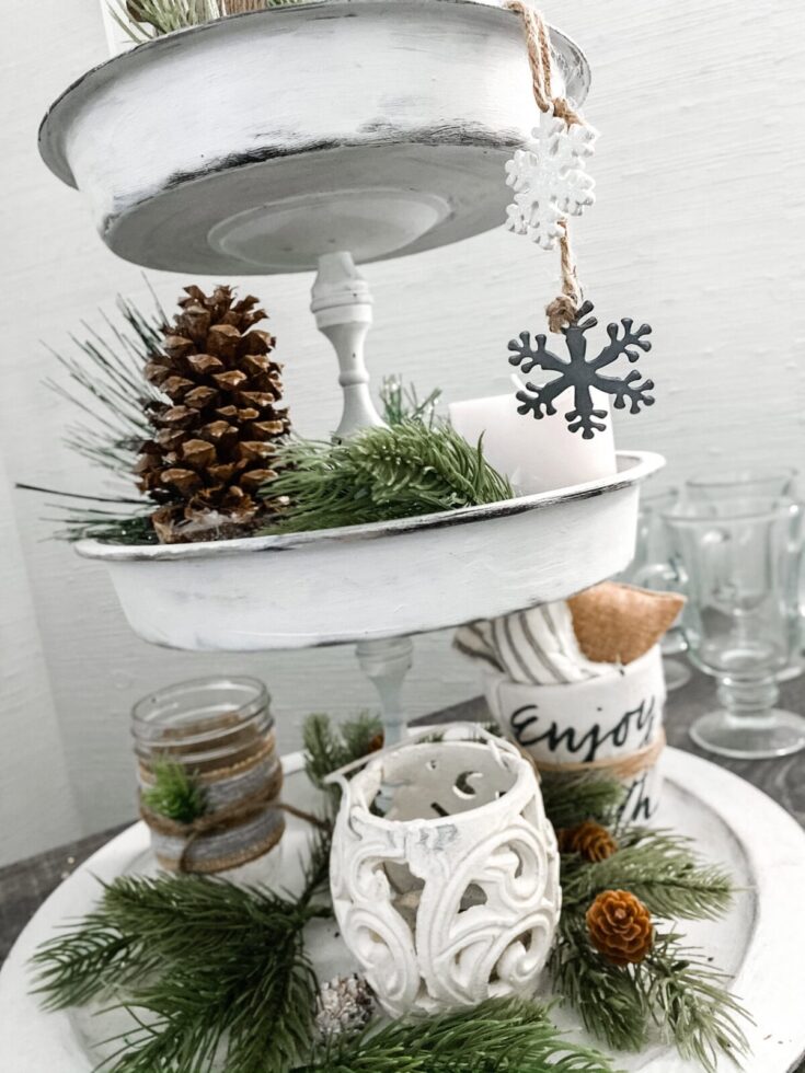 Pinecone, snowflake ornament, and festive greenery on a tiered white wooden tray Christmas centerpiece.
