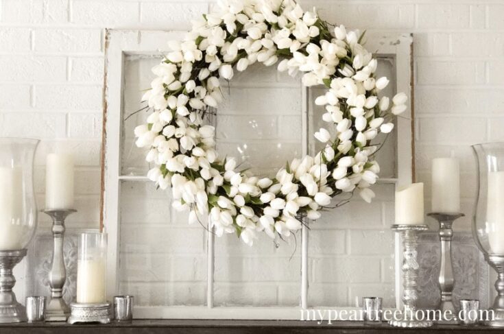 White floral wreath with tulips displayed against a white brick wall, perfect for elegant home decor or wedding decoration.