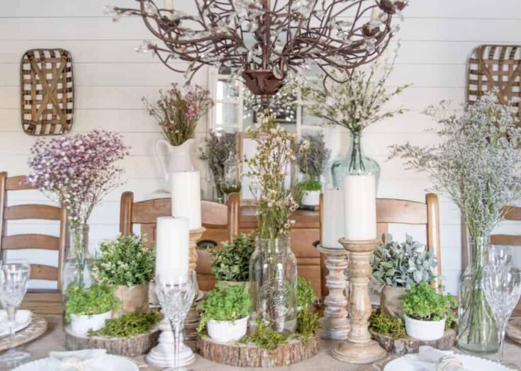 Soft pastel flower arrangements with greenery and candles on a rustic wooden dining table, perfect for spring or summer gatherings.